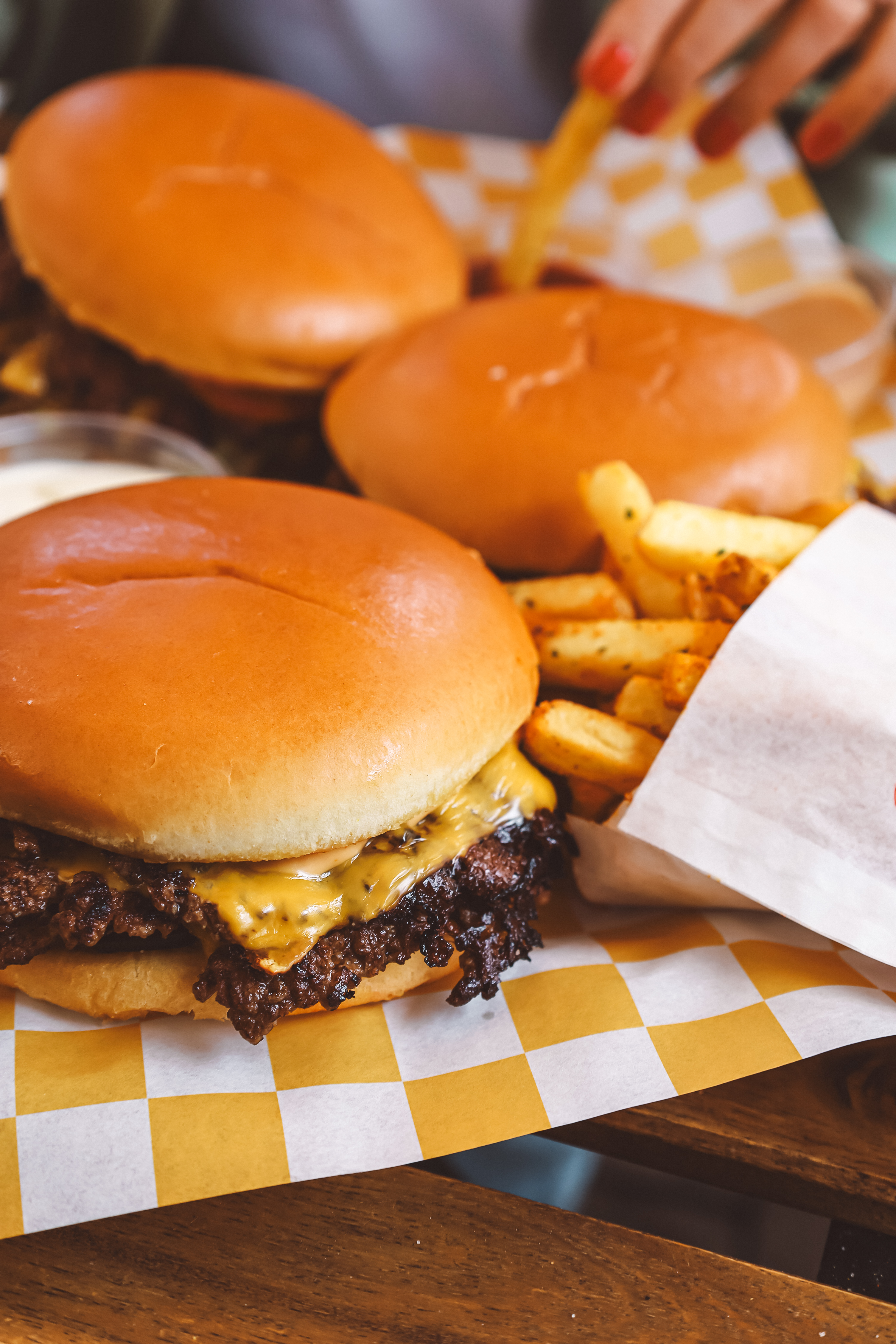 Három burger és sültkrumpli fa asztalon